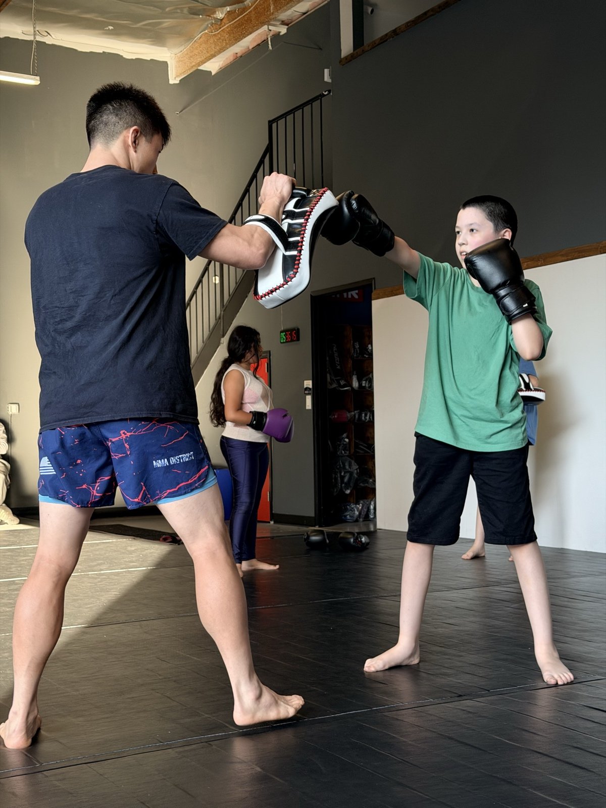 A young student throwing a punch on the pads with a coach in the MMA District youth class