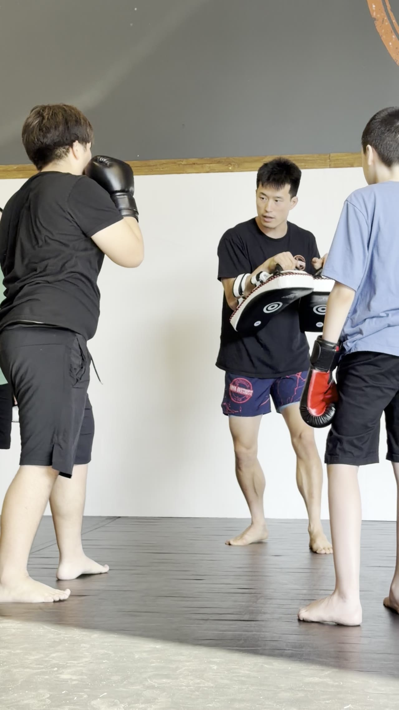 A coach holding pads for two young students during a kickboxing drill at MMA District